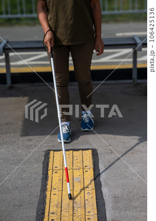 Close-up of the legs of an elderly blind woman at a bus stop. 106425136