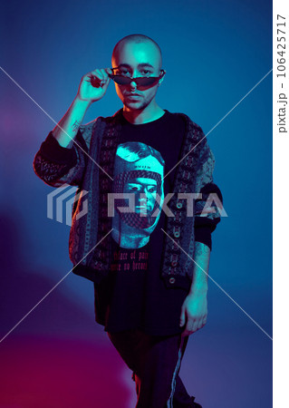 Studio shot of a young tattoed bald man posing against a colorful background. 90s style. Studio shot of a young tattoed bald man posing against a colorful background. 90s style. 106425717