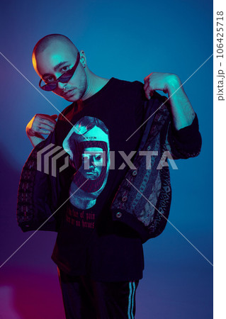 Studio shot of a young tattoed bald man posing against a colorful background. 90s style. Studio shot of a young tattoed bald man posing against a colorful background. 90s style. 106425718