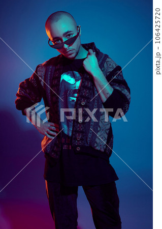 Studio shot of a young tattoed bald man posing against a colorful background. 90s style. Studio shot of a young tattoed bald man posing against a colorful background. 90s style. 106425720