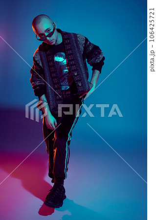 Studio shot of a young tattoed bald man posing against a colorful background. 90s style. Studio shot of a young tattoed bald man posing against a colorful background. 90s style. 106425721