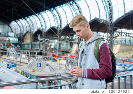 Young guy using mobile apps on smartphone standing at railway station Young guy using mobile apps on smartphone standing at railway station 106427623