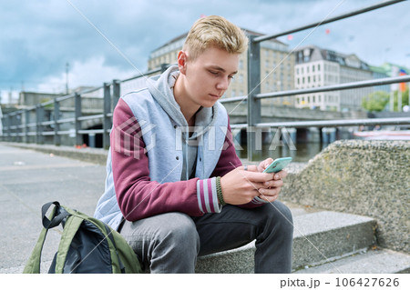 Serious guy college student using smart phone sitting on city river embankment 106427626