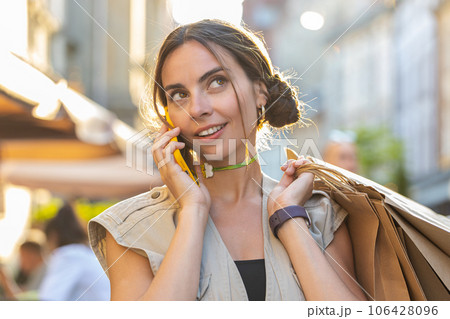 Woman shopaholic consumer after shopping sale with full bags with gifts outdoors, talking on phone 106428096