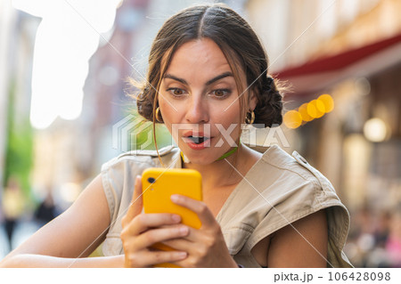 Excited happy winner young woman use smartphone celebrating win good message news in city street Excited happy winner young woman use smartphone celebrating win good message news in city street 106428098