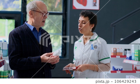 Adept pharmacy heart specialist helping aged man with medical counsel. Older client in dispensary wishing to purchase heartbeat regulating drugs, asking expert for guidance 106429243