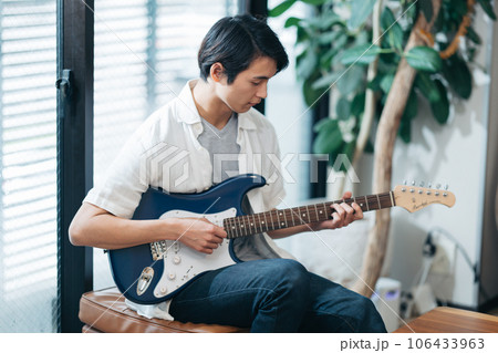 自宅でギターの練習をする若い男性 106433963