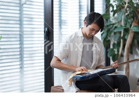 自宅でギターの手入れをする若い男性 106433964