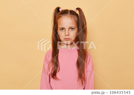 Upset unhappy little girl with ponytails wearing pink sweatshirt isolated over beige background looking at camera with pout lips being offended expressing negative emotions. 106435545