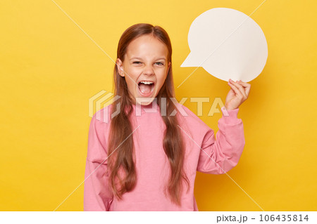 Dialog in an empty speech bubble. Creative idea on a blank card. Excited amazed little girl with long hair holding empty speech bubble wearing pink sweatshirt isolated over yellow background 106435814