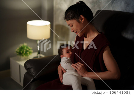 mother breastfeeding infant baby on sofa in the living room at night 106441082