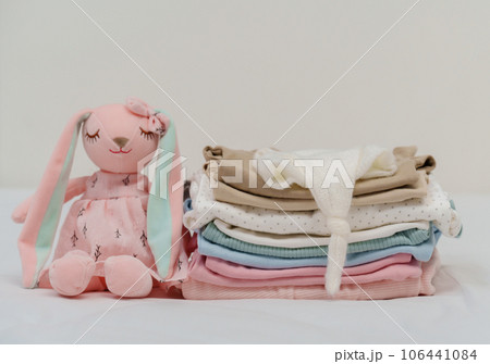 stack of baby clothes and toy on bed 106441084