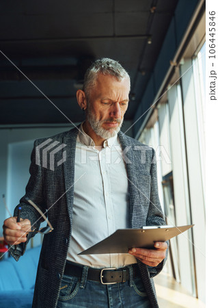 Focused businessman looking on documents and think how to solve problem while standing in office Focused businessman looking on documents and think how to solve problem while standing in office 106445846