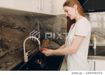 A housewife woman washes dishes in the kitchen in the sink. A housewife woman washes dishes in the kitchen in the sink. 106446450