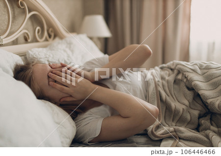 Young woman suffering with headache flu ill sick disease cold at home indoor lying on bed top view 106446466