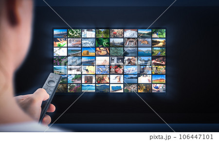 TV online. Multimedia streaming concept. Hand holding remote control. TV screen with lot of pictures. Person relaxing at home in evening TV online. Multimedia streaming concept. Hand holding remote control. TV screen with lot of pictures. Person relaxing at home in evening 106447101