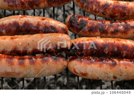 Grilled sausages. Cook man preparing grilling food bbq. Barbecue with smoke, flame outdoors. Tasty juicy german bratwurst. Charcoal kettle grill outside in backyard. Family summer vacation. Close-up Grilled sausages. Cook man preparing grilling food bbq. Barbecue with smoke, flame outdoors. Tasty juicy german bratwurst. Charcoal kettle grill outside in backyard. Family summer vacation. Close-up 106448049