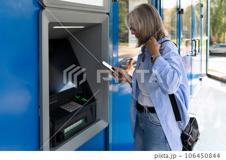 a mature adult woman stands near an ATM on a city street a mature adult woman stands near an ATM on a city street 106450844