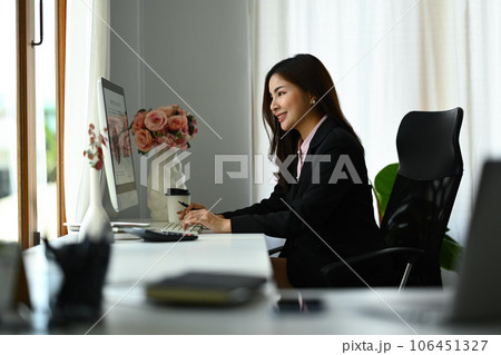 Side view of successful asian woman investor looking at computer monitor, working on investment and marketing projects at office 106451327
