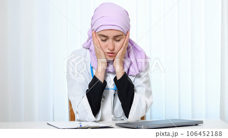 Muslim woman in doctor suit works with tired expression Muslim woman in doctor suit works with tired expression 106452188