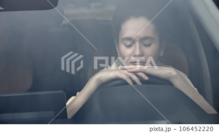 Woman sits in car with sad expression view through windshield Woman sits in car with sad expression view through windshield 106452220