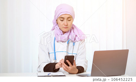Practitioner in hijab types messages to patient on phone 106452225