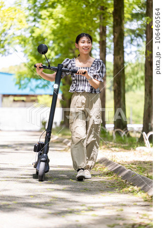 爽やかな木漏れ日の中を電動キックボードで散策する若くてかわいい女性｜電動キックボードイメージ 106460564