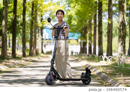 爽やかな木漏れ日の中を電動キックボードで散策する若くてかわいい女性|電動キックボードイメージ 爽やかな木漏れ日の中を電動キックボードで散策する若くてかわいい女性|電動キックボードイメージ 106460574