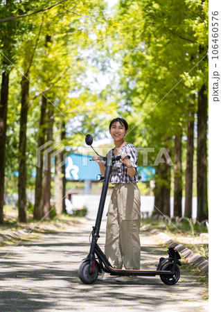 爽やかな木漏れ日の中を電動キックボードで散策する若くてかわいい女性｜電動キックボードイメージ 106460576