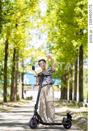 爽やかな木漏れ日の中を電動キックボードで散策する若くてかわいい女性｜電動キックボードイメージ 106460578