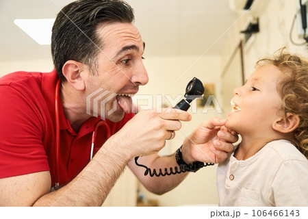 Pediatrician doctor examining child. Male doctor examining boy's ear with otoscope in hospital. 106466143