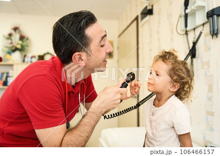 Pediatrician doctor examining child. Male doctor examining boy's ear with otoscope in hospital. Pediatrician doctor examining child. Male doctor examining boy's ear with otoscope in hospital. 106466157