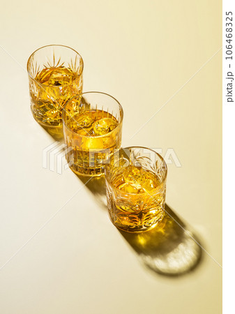 Three whiskey glasses with ice cubes on golden background. Three whiskey glasses with ice cubes on golden background. 106468325