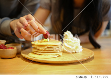 Closeup shot of woman decorating pancake with fresh strawberries, young couple preparing breakfast in the kitchen 106470599