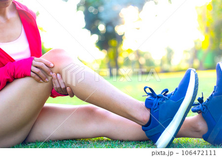Girl sitting on green grass in the park . Knee pain from incorrect exercise. from strenuous exercise. Most of the symptoms are in people who are overweight. sunset light background Girl sitting on green grass in the park . Knee pain from incorrect exercise. from strenuous exercise. Most of the symptoms are in people who are overweight. sunset light background 106472111