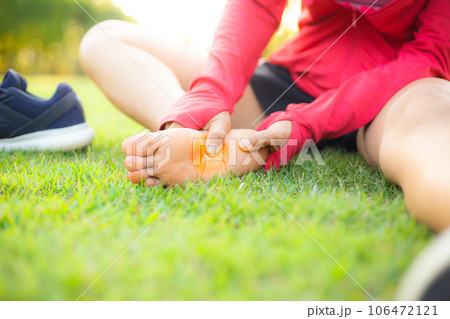 Girl sitting on green grass in the park. Foot pain from the wrong exercise .Symptoms of peripheral neuropathy. Most symptoms are numbness in the fingertips and foot. sun set light background. Girl sitting on green grass in the park. Foot pain from the wrong exercise .Symptoms of peripheral neuropathy. Most symptoms are numbness in the fingertips and foot. sun set light background. 106472121
