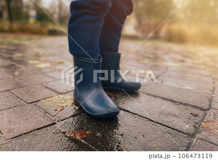 Close-up of a child in rubber boots on wet pavement after rain 106473119