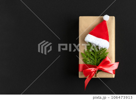 Craft gift box with christmas tree made of thuja and santa hat on dark background with space for your text. Craft gift box with christmas tree made of thuja and santa hat on dark background with space for your text. 106473913