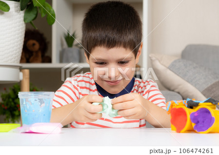 A six-year-old boy plays with slime while sitting at a table at home. A toy for the development of fine motor skills and creativity in children 106474261