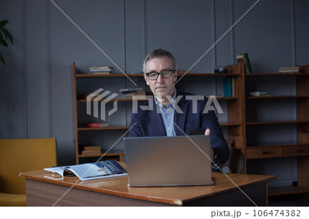 Portrait of mature businessman in suit pensivly working on the laptop in his office Portrait of mature businessman in suit pensivly working on the laptop in his office 106474382