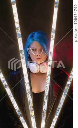 Cyberpunk people. Futuristic portrait. Vaporwave party night. Confident DJ woman with blue hair goggles headphones on pink neon light glitch illumination smoke dark background. Cyberpunk people. Futuristic portrait. Vaporwave party night. Confident DJ woman with blue hair goggles headphones on pink neon light glitch illumination smoke dark background. 106474749