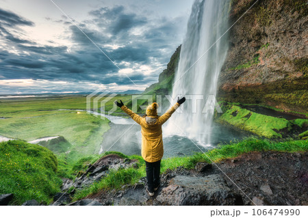 Seljalandsfoss waterfall flowing from cliff with cheerful tourist woman standing in summer at Iceland Seljalandsfoss waterfall flowing from cliff with cheerful tourist woman standing in summer at Iceland 106474990