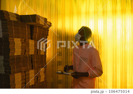 African male employee checking with clipboard at stacked cardboard package stuck in shipping warehouse at manufacturing factory African male employee checking with clipboard at stacked cardboard package stuck in shipping warehouse at manufacturing factory 106475014