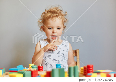 Creating learning environment. Playful games for curious minds. Child's educational playtime funny curious wavy haired blonde toddler baby playing wooden educational toys isolated over gray background 106476785