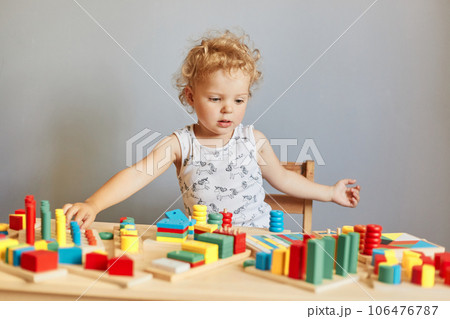 Building blocks of learning. Child's playful journey of discovery. Curious child's playful learning. Wavy haired blonde infant baby playing wooden educational toys isolated over gray background 106476787