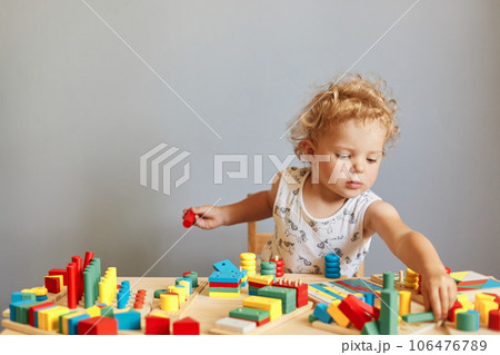 Childhood curiosity and discovery. Playful games for curious minds. Cute creative wavy haired blonde toddler baby playing wooden educational toys isolated over gray background Childhood curiosity and discovery. Playful games for curious minds. Cute creative wavy haired blonde toddler baby playing wooden educational toys isolated over gray background 106476789
