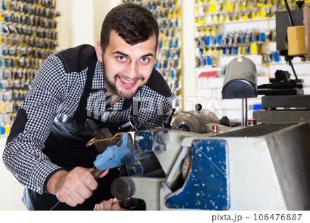 male worker shaping new key in repair workshop 106476887