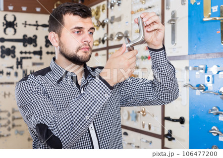 friendly male customer examining various door handles in store 106477200