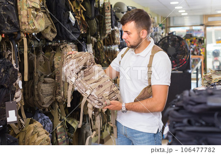 guy looking camouflage backpack in army store 106477782