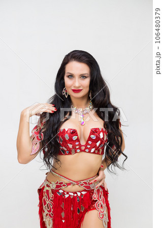 A brunette girl in a red dance costume performs oriental dances, a gray background A brunette girl in a red dance costume performs oriental dances, a gray background 106480379